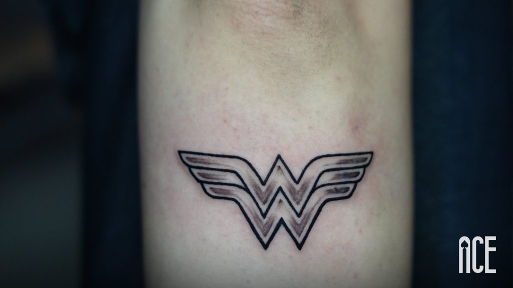 Tatuaj fine line cu simbolul Wonder Woman pe antebraț, lucrare realizată la Ace Tattoo Parlour din București