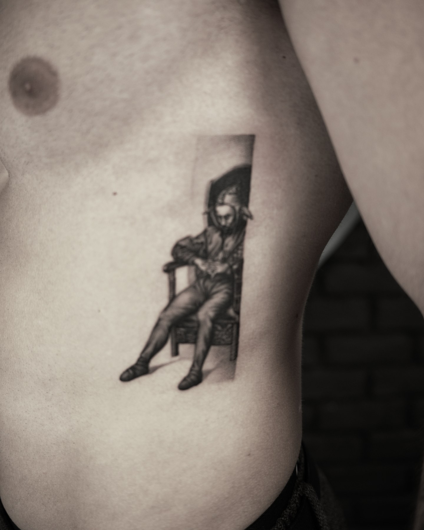 Bărbat așezat pe scaun, gravură pe coaste, tatuaj black and grey de Rox la Ace Tattoo București